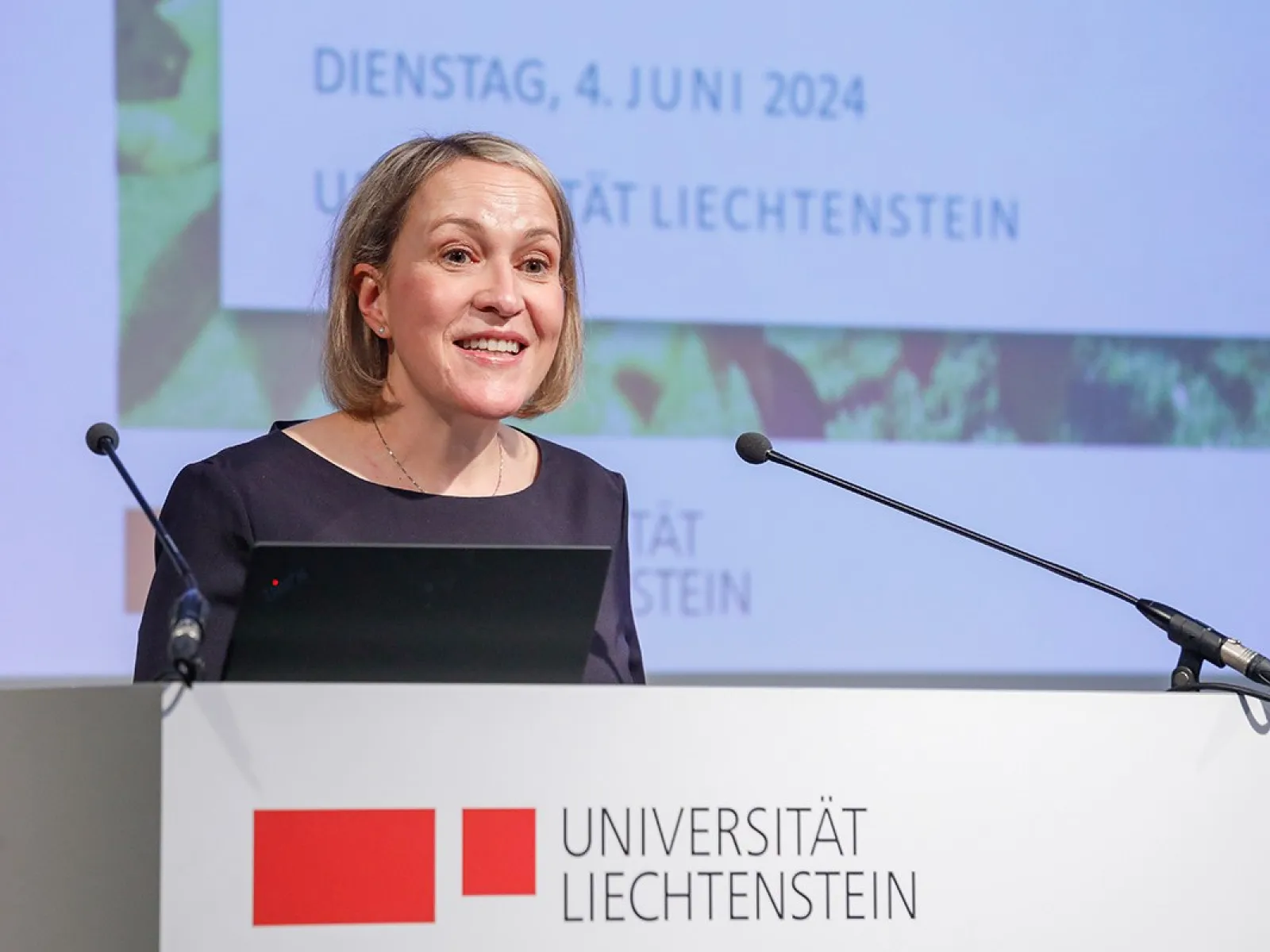 Eine Frau hält eine Rede am Rednerpult der Universität Liechtenstein. Im Hintergrund ist eine Präsentationsfolie mit dem Datum 4. Juni 2024 zu sehen.