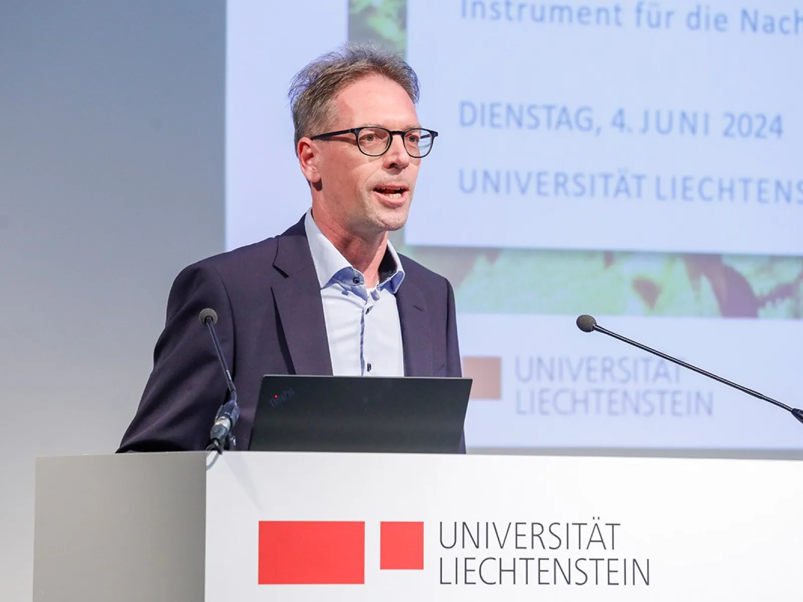 Ein Mann hält einen Vortrag im Auditorium der Universität Liechtenstein. Im Hintergrund ist eine Präsentation mit dem Datum 4. Juni 2024 zu sehen. Ein Rednerpult mit dem Logo der Universität steht vor ihm.