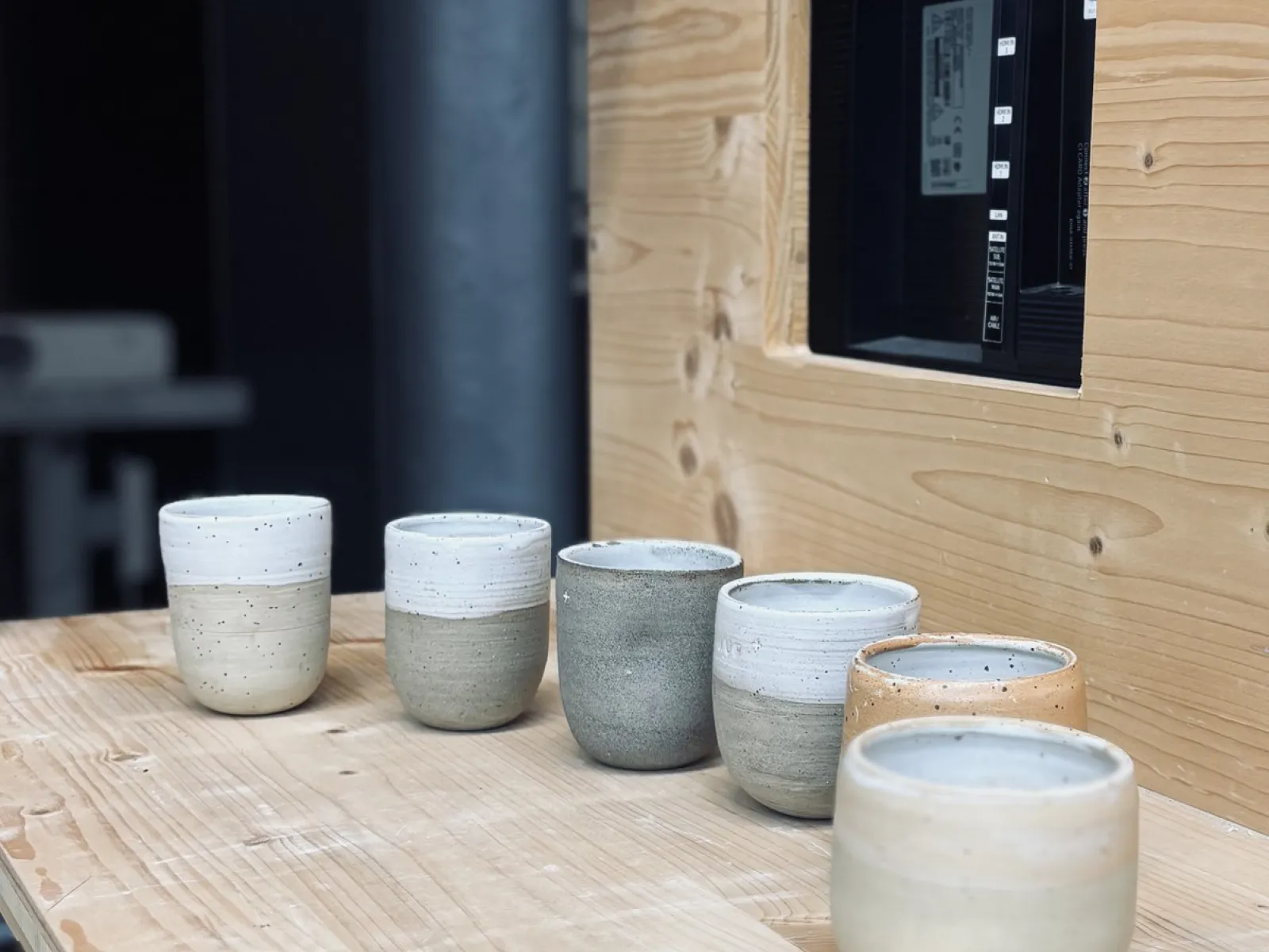 Sechs handgetöpferte Keramiktassen in verschiedenen Erdtönen stehen auf einem Holztisch. Die Tassen sind schlicht und modern gestaltet, passend zur Architekturveranstaltung an der Universität Liechtenstein.