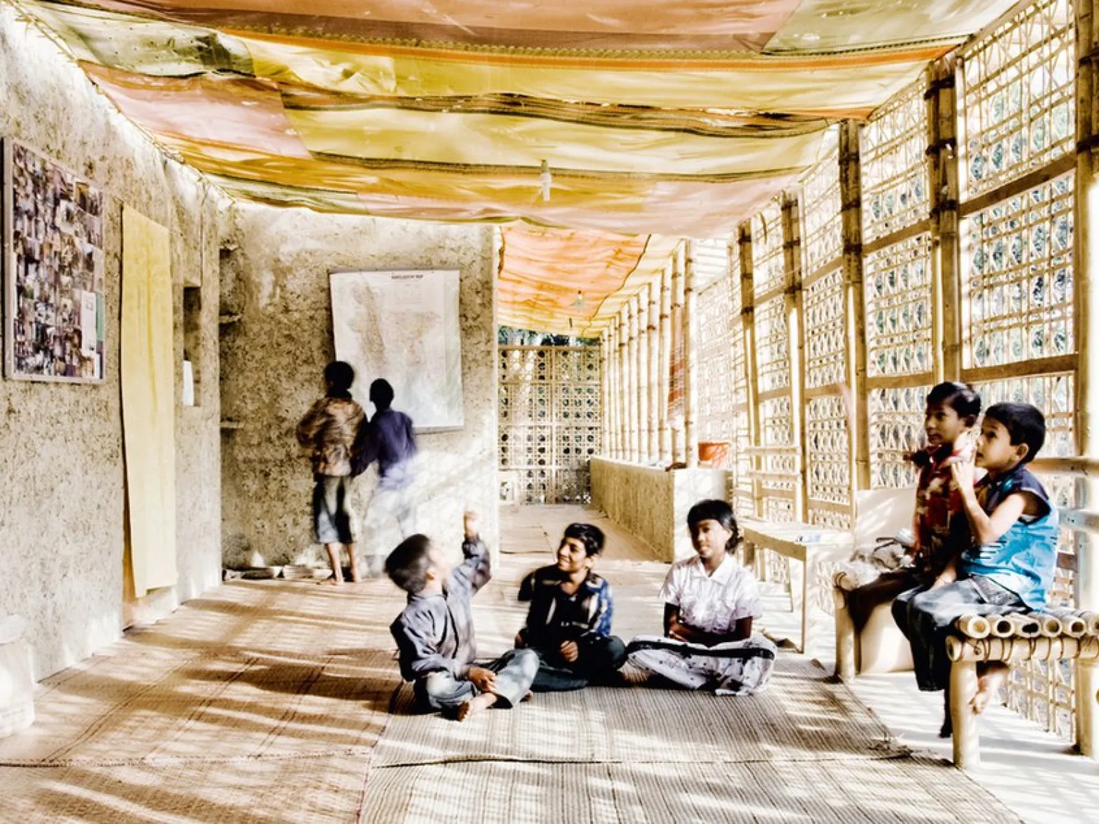 Ein heller Korridor mit Wänden aus natürlichen Materialien wie Lehm und Bambus. Kinder sitzen und stehen entspannt im Raum, der mit bunten Stoffen dekoriert ist. Die Architektur verbindet traditionelle Bauweisen mit modernem Design.