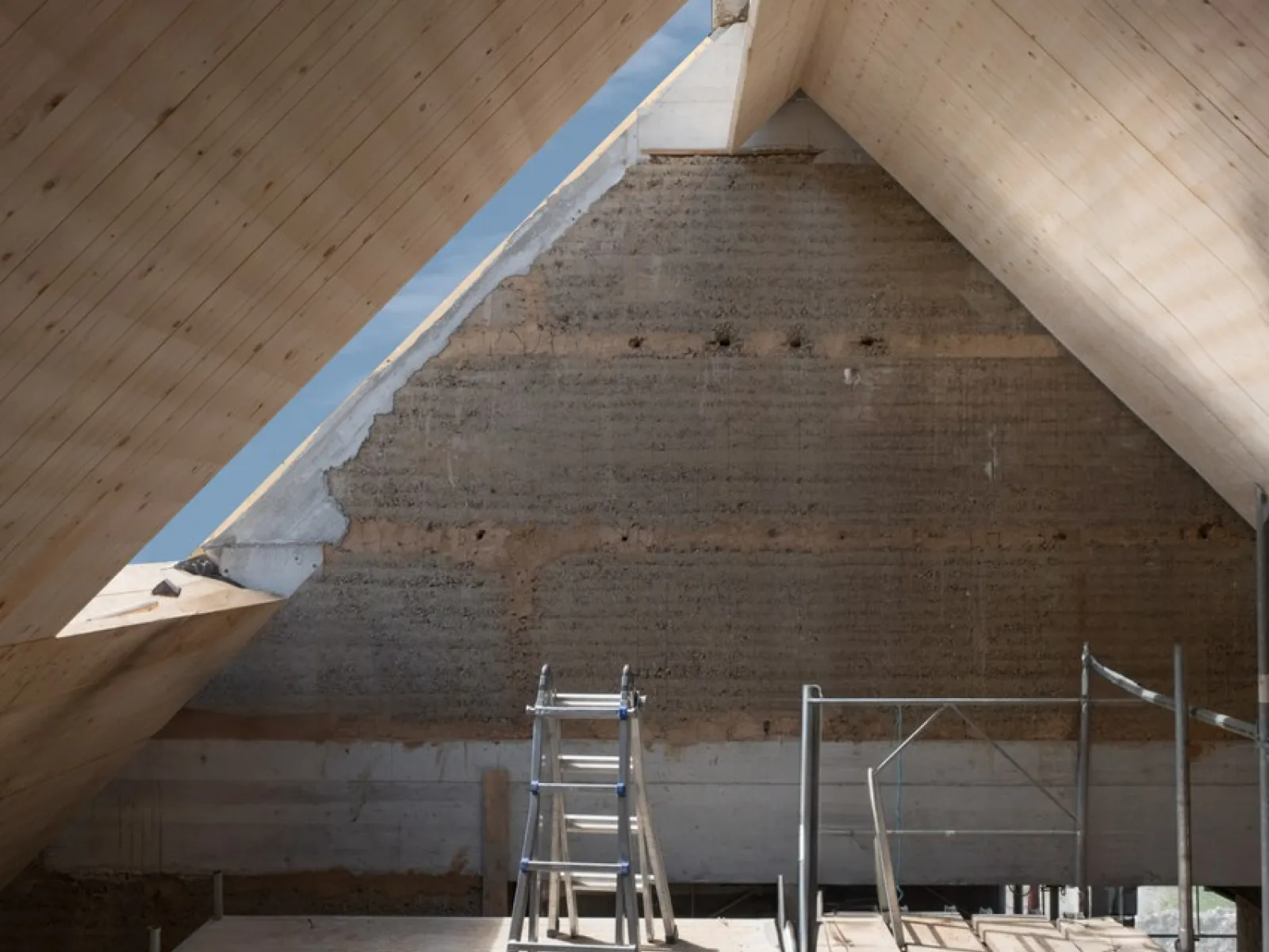 Innenansicht eines Dachbodens in Renovierung mit sichtbarer Holzkonstruktion und Gerüst. Natürliches Licht fällt durch ein Dachfenster.