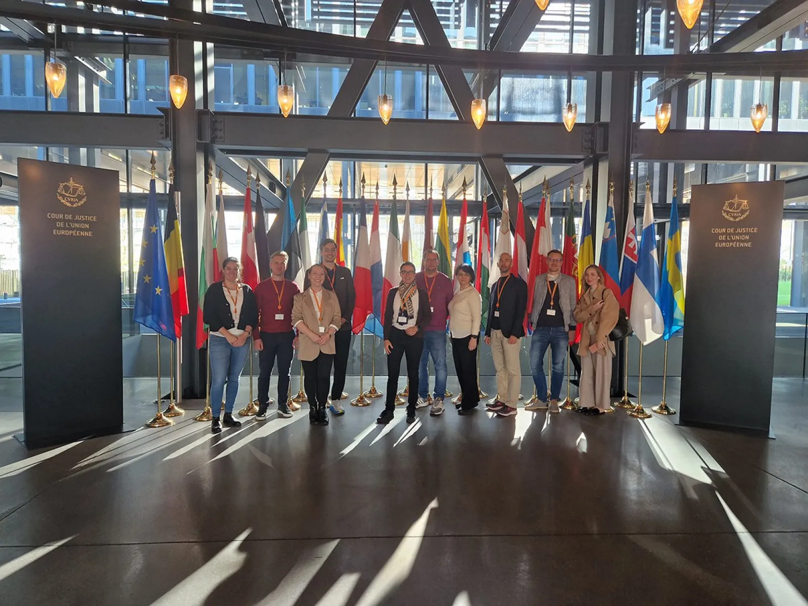 Gruppe von Studierenden des Executive Master of Laws (LL.M.) im Wirtschaftsstrafrecht steht vor einer Reihe internationaler Flaggen im Gebäude des Internationalen Strafgerichtshofs in Den Haag.