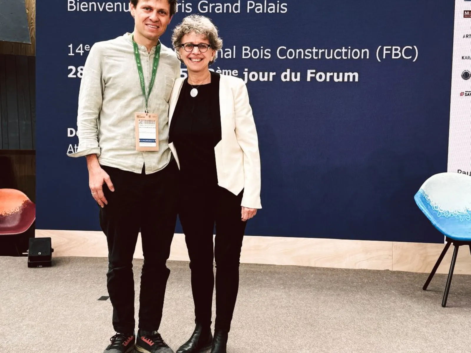 Zwei Personen stehen auf einer Bühne vor einem blauen Banner mit der Aufschrift „Forum Bois Construction“ im Grand Palais, Paris. Sie lächeln in die Kamera.