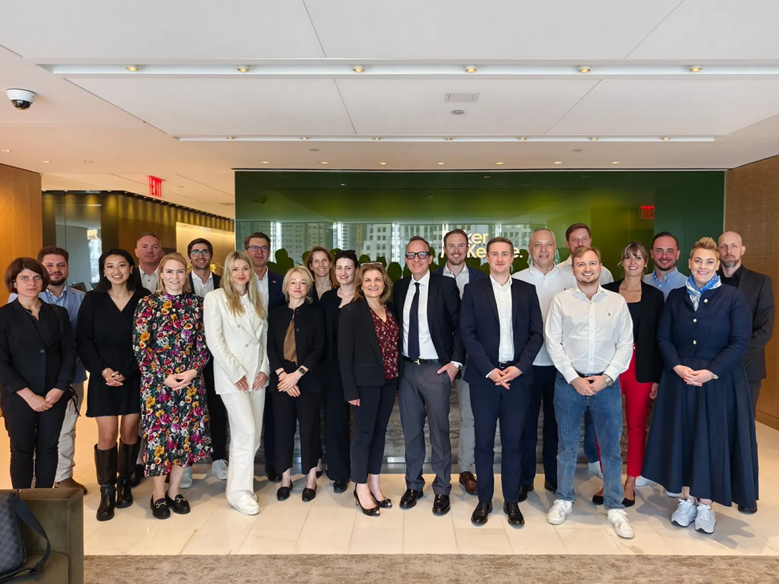 Eine Gruppe von Studierenden und Dozenten des Executive Master of Laws (LL.M.) der Universität Liechtenstein posiert in einem modernen Konferenzraum während ihrer Studienreise in New York. Sie stehen in formeller Kleidung vor einer Glaswand, die das Logo einer Anwaltskanzlei zeigt.