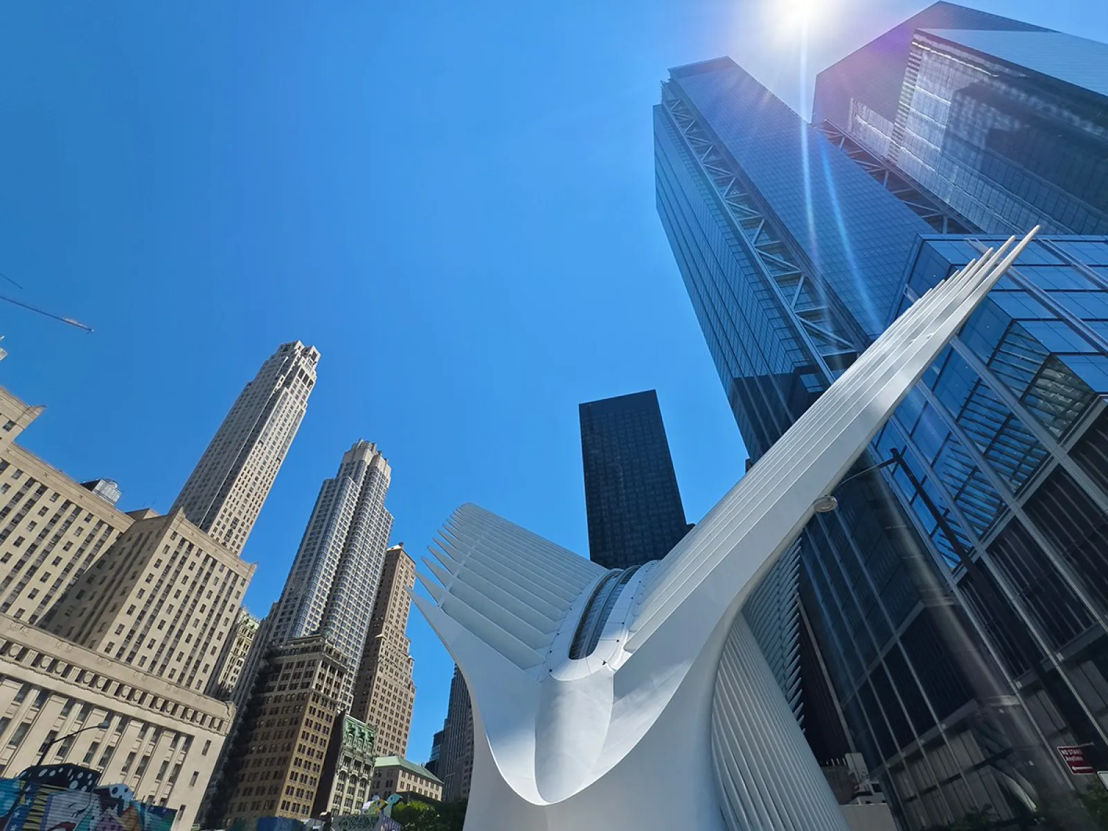 Blick auf moderne Wolkenkratzer und das Oculus-Gebäude in New York City bei strahlend blauem Himmel.