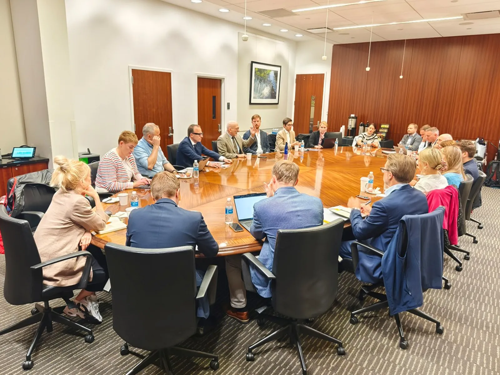 Eine Gruppe von Studierenden und Dozenten sitzt in einem Konferenzraum an einem großen, ovalen Tisch. Sie sind in einer Besprechung vertieft, umgeben von Büromöbeln und moderner Einrichtung.
