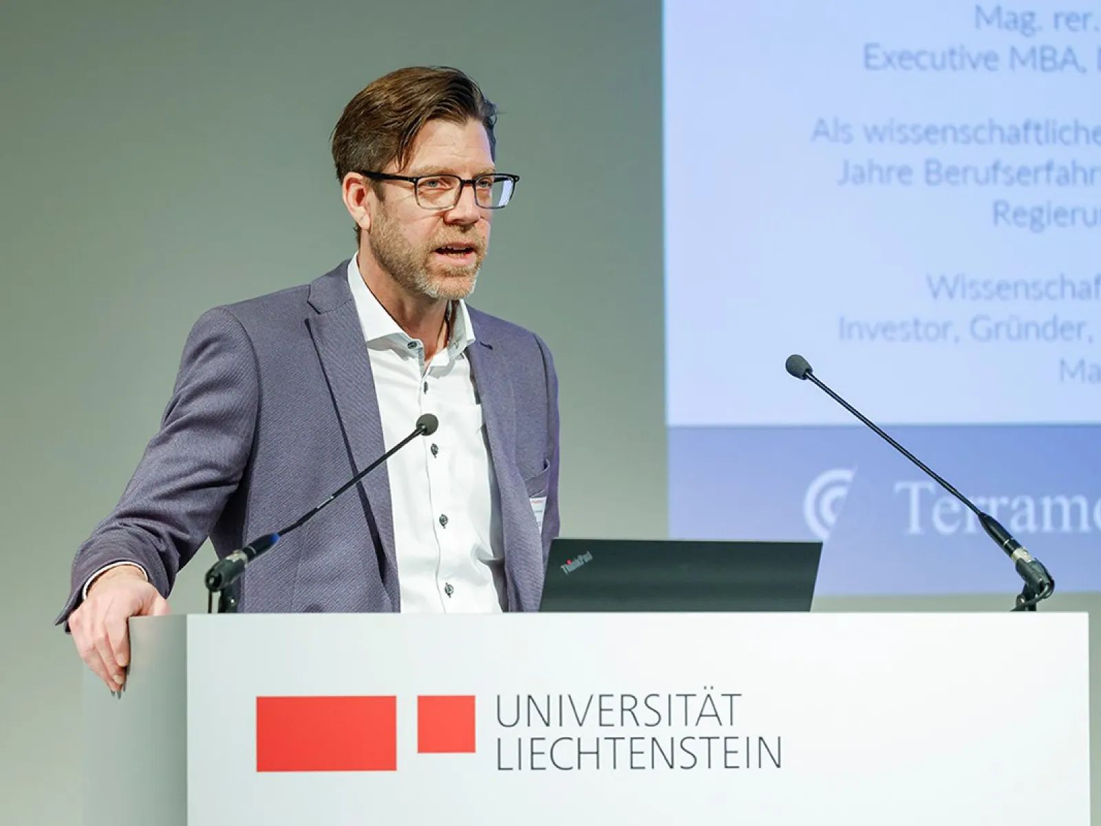 Ein Mann hält einen Vortrag an einem Rednerpult der Universität Liechtenstein. Im Hintergrund ist eine Präsentation zu sehen.