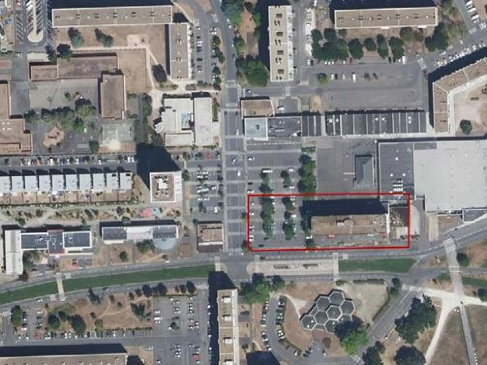 Luftbild einer städtischen Umgebung mit mehreren Gebäuden und Straßen. Ein Bereich ist rot umrandet, möglicherweise zur Hervorhebung eines spezifischen Projekts oder Standorts.
