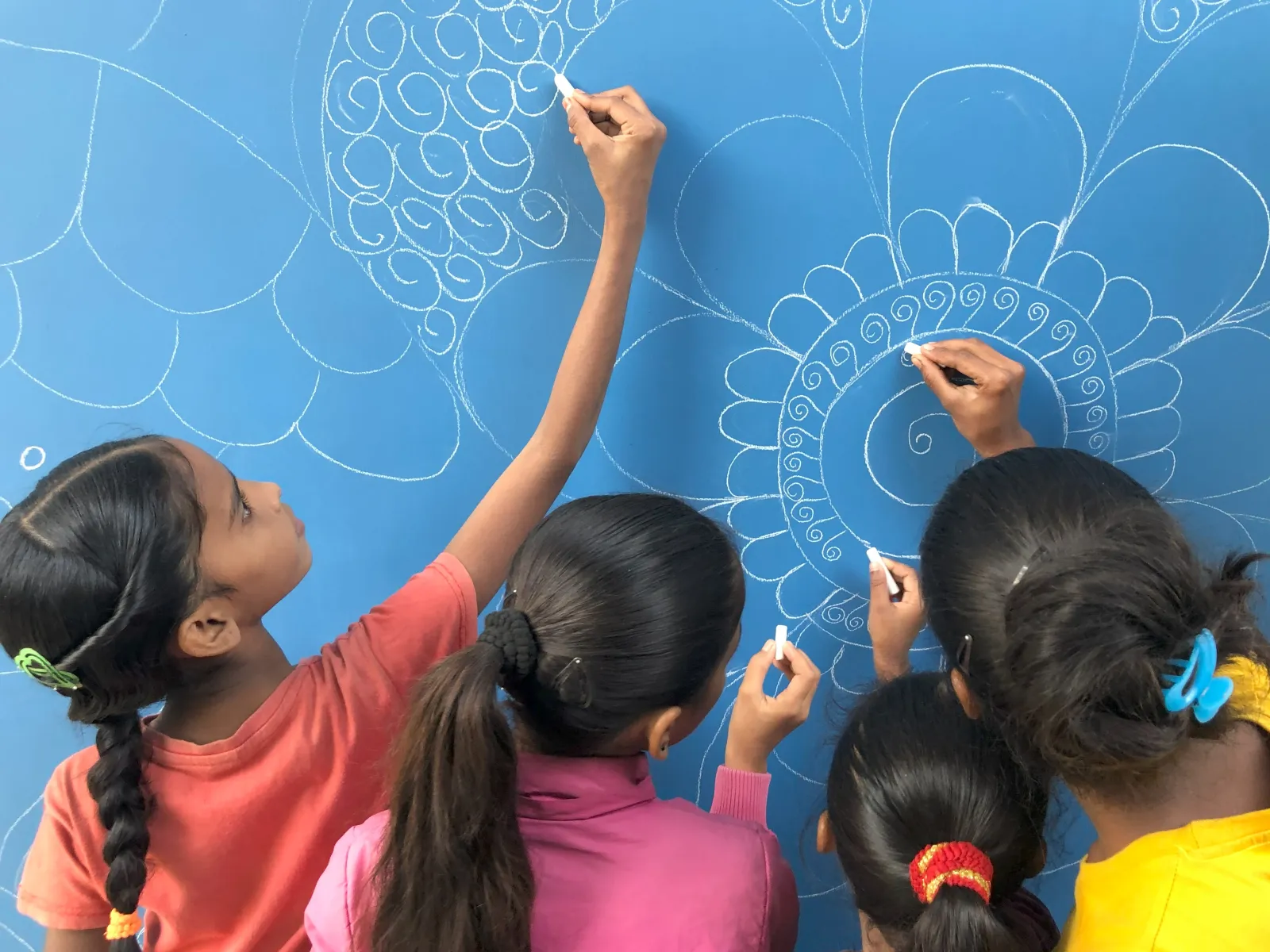 Mehrere Kinder zeichnen mit Kreide ein großes, ornamentales Muster auf eine blaue Tafel.