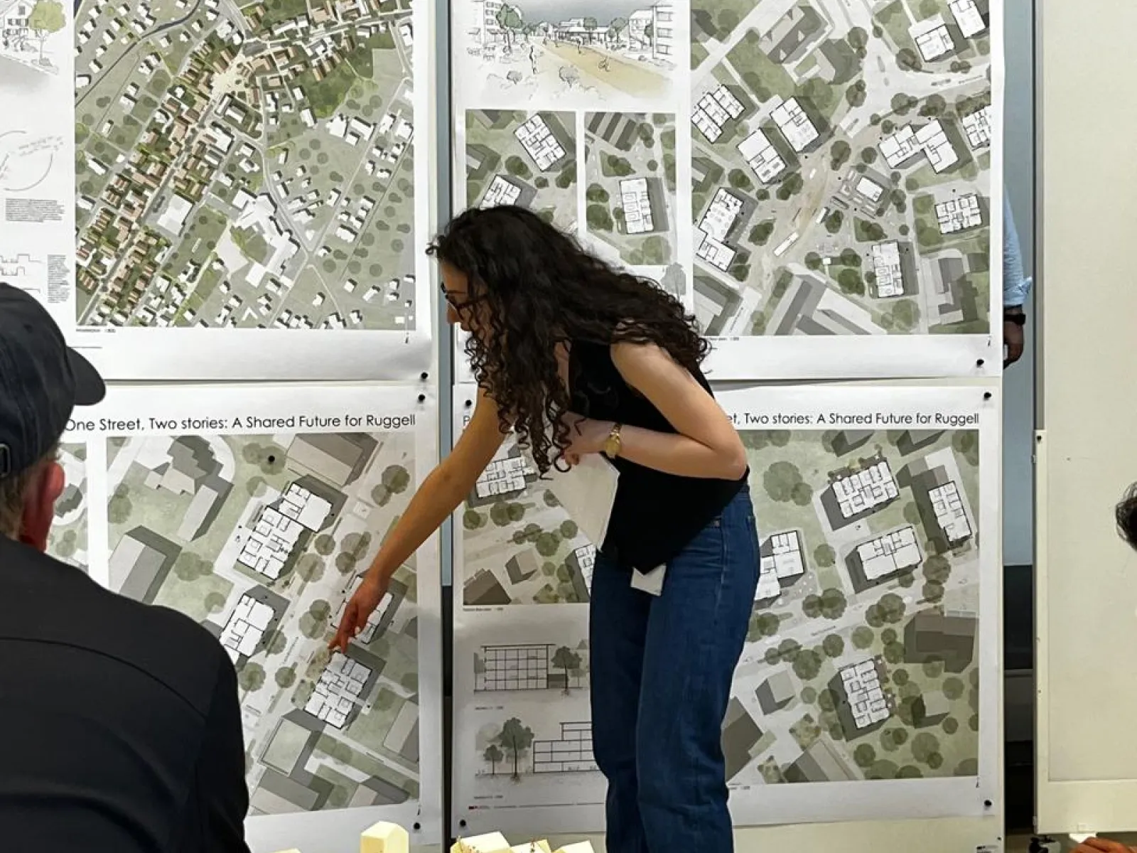 Studentin in Präsentationssituation mit Plänen im Hintergrund