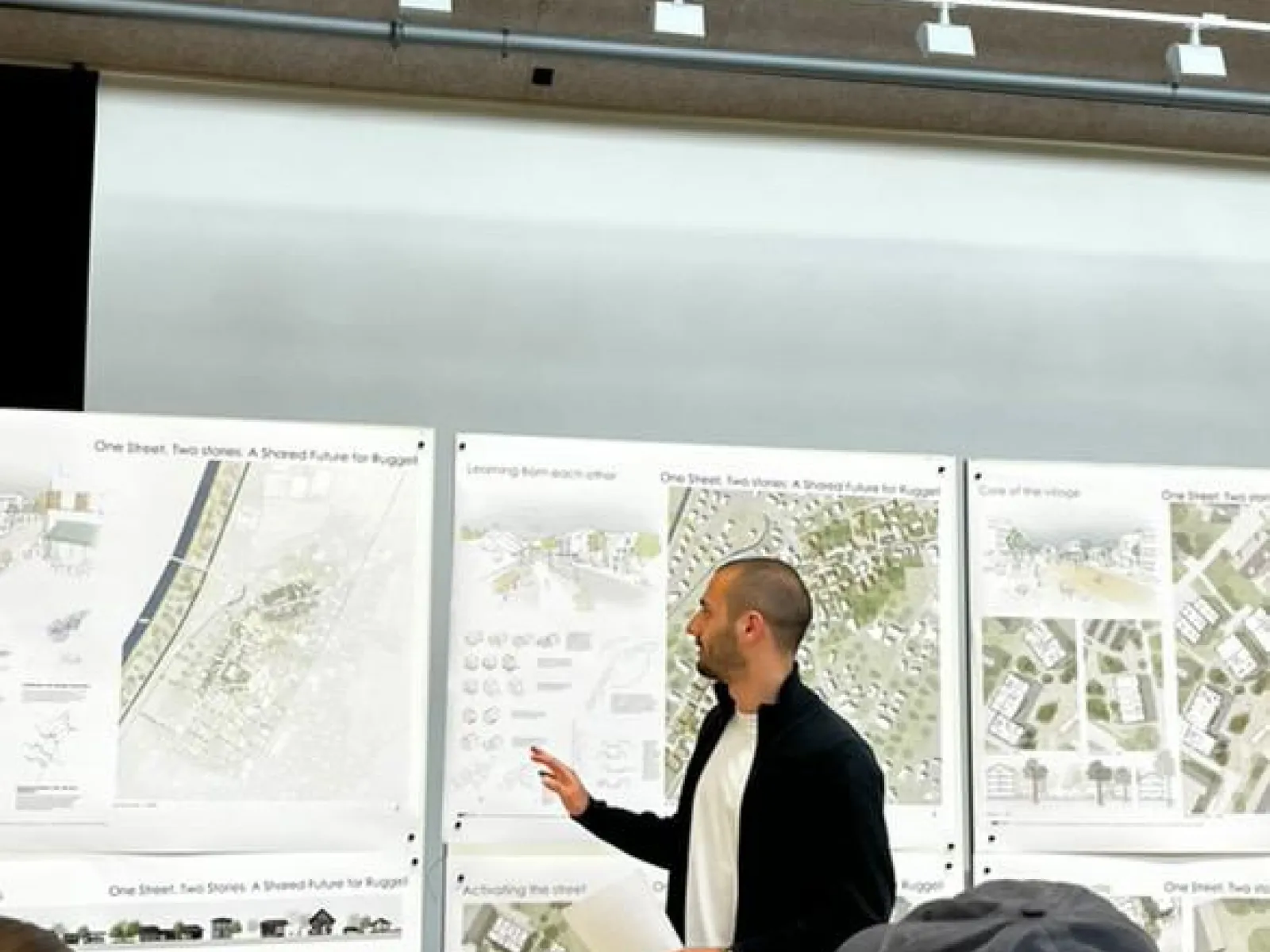 Student in Präsentationssituation mit Plänen im Hintergrund