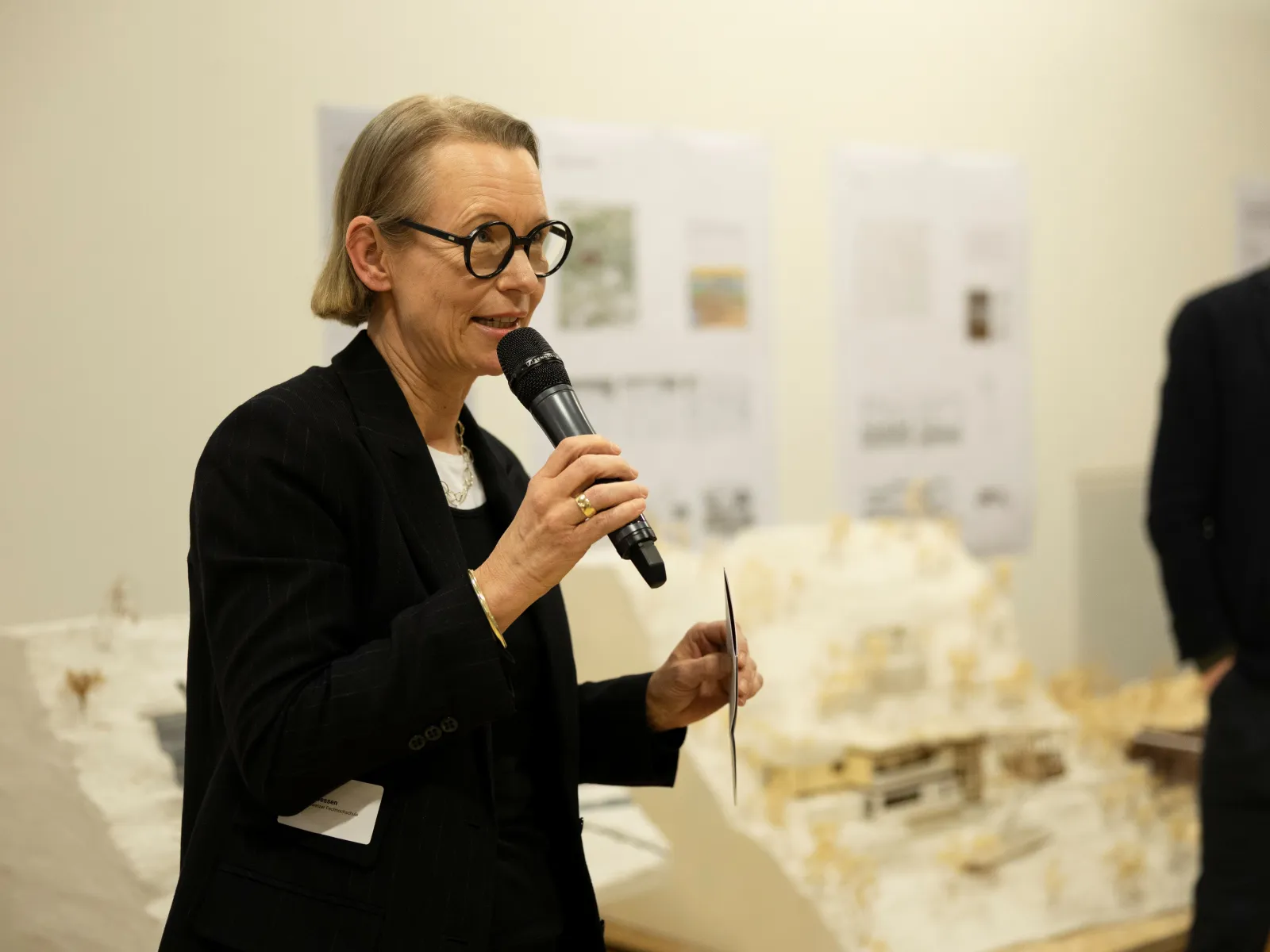 Eine Frau mit schwarzem Sakko und Brille spricht in ein Mikrofon