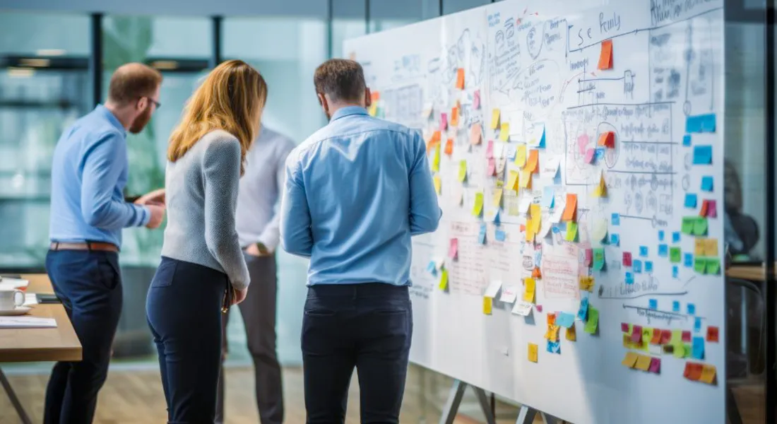 Teilnehmende eines Workshops an der Universität Liechtenstein stehen vor einem Whiteboard mit bunten Post-its und grafischen Konzepten.