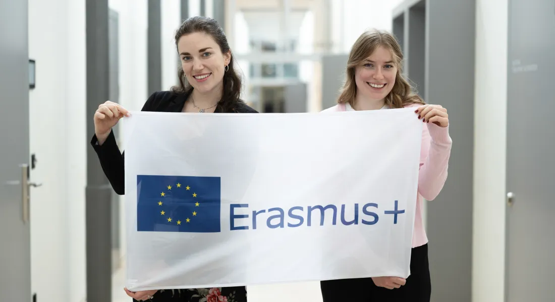Zwei Studentinnen halten Erasmus-Plus-Flagge im Uni-Gebäude.