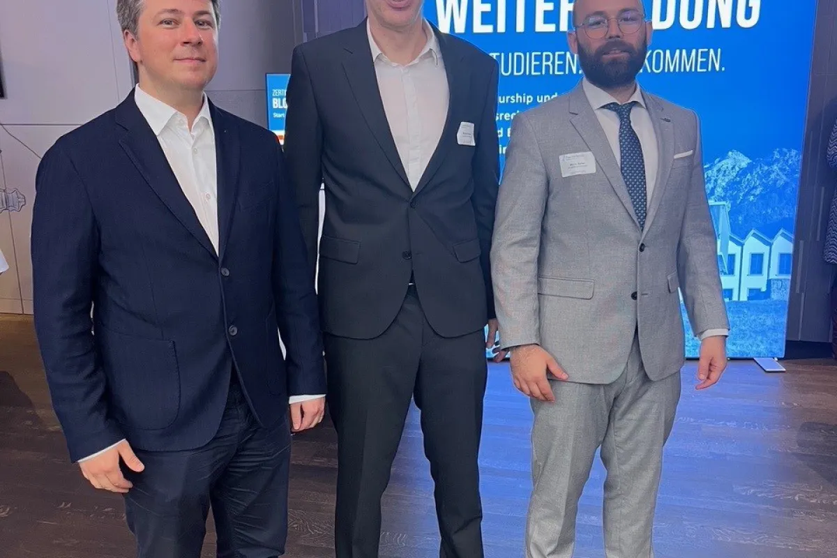 Drei Männer in Anzügen stehen vor einem Schild der Universität Liechtenstein. Im Hintergrund ist ein Banner mit der Aufschrift "Weiterbildung" zu sehen.