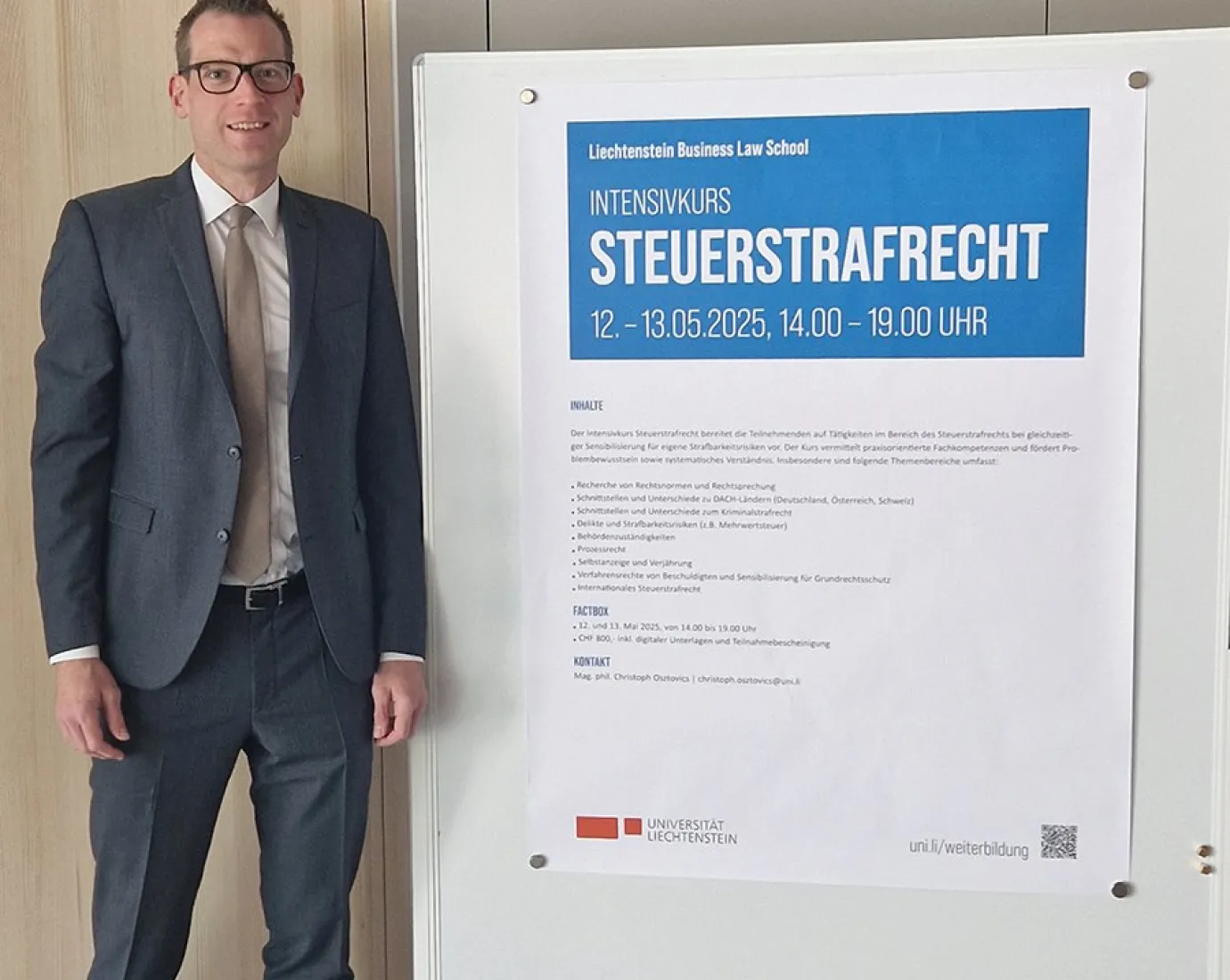 Ein Mann in Anzug steht neben einem Plakat, das den Intensivkurs „Steuerstrafrecht“ der Universität Liechtenstein ankündigt. Das Plakat enthält Informationen zu Datum, Uhrzeit und Inhalten des Kurses.