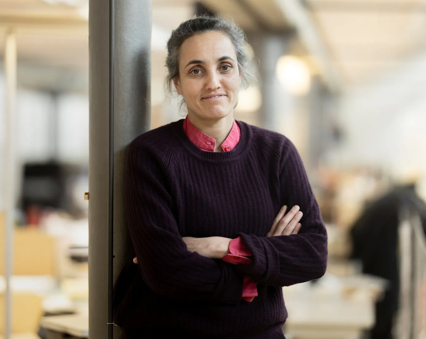 Porträt einer Frau mit schwarzem Pullover, die mit verschränkten Armen an einer Säule lehnt