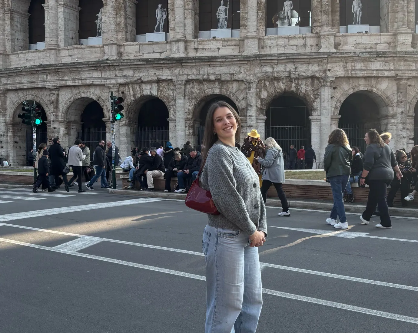 Frau steht lächelnd vor dem Kolosseum, während im Hintergrund Touristen an der Straße entlanggehen.