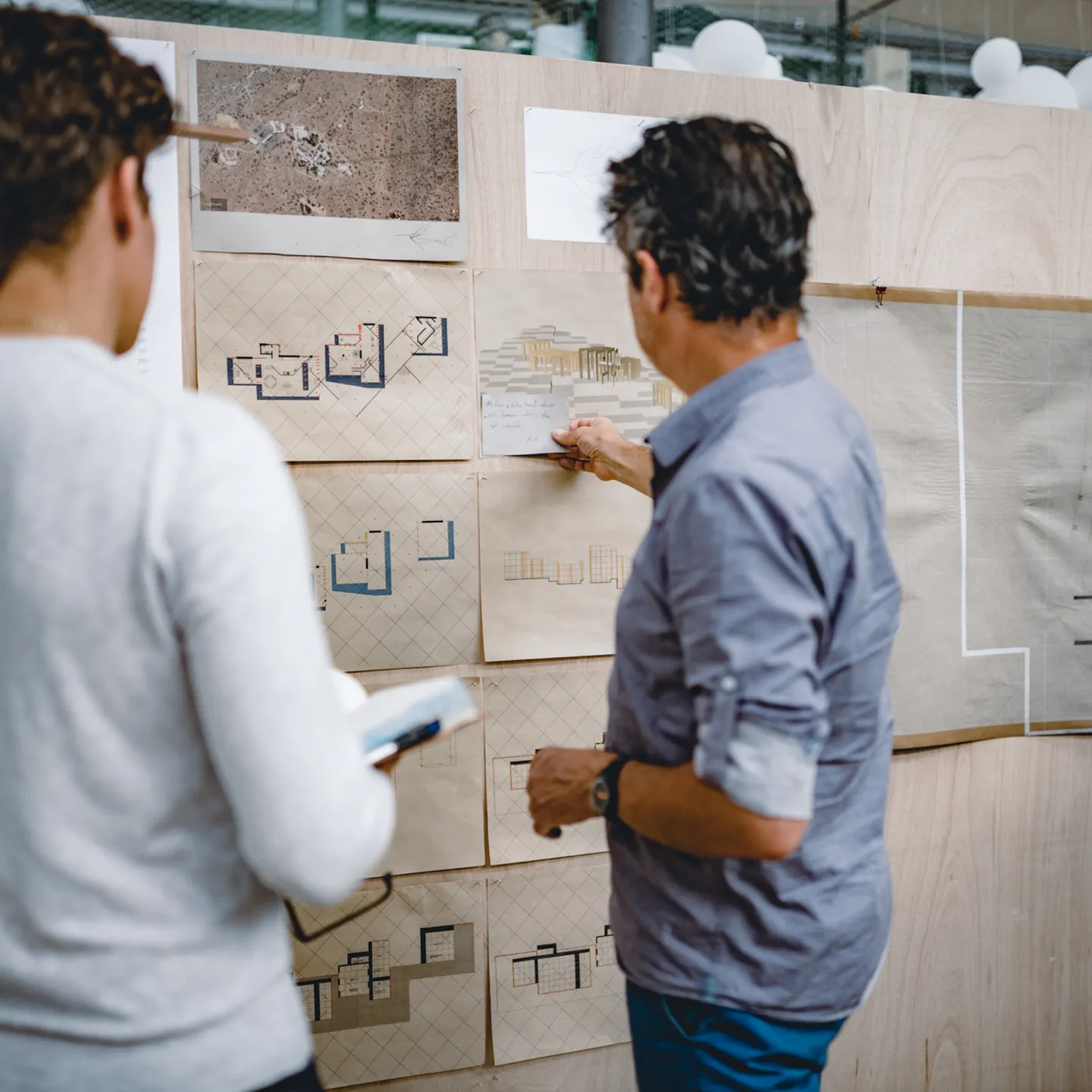 Dozent und Student besprechen architektonische Pläne an einer Präsentationswand – individuelle Betreuung im Designstudium an der Universität Liechtenstein.