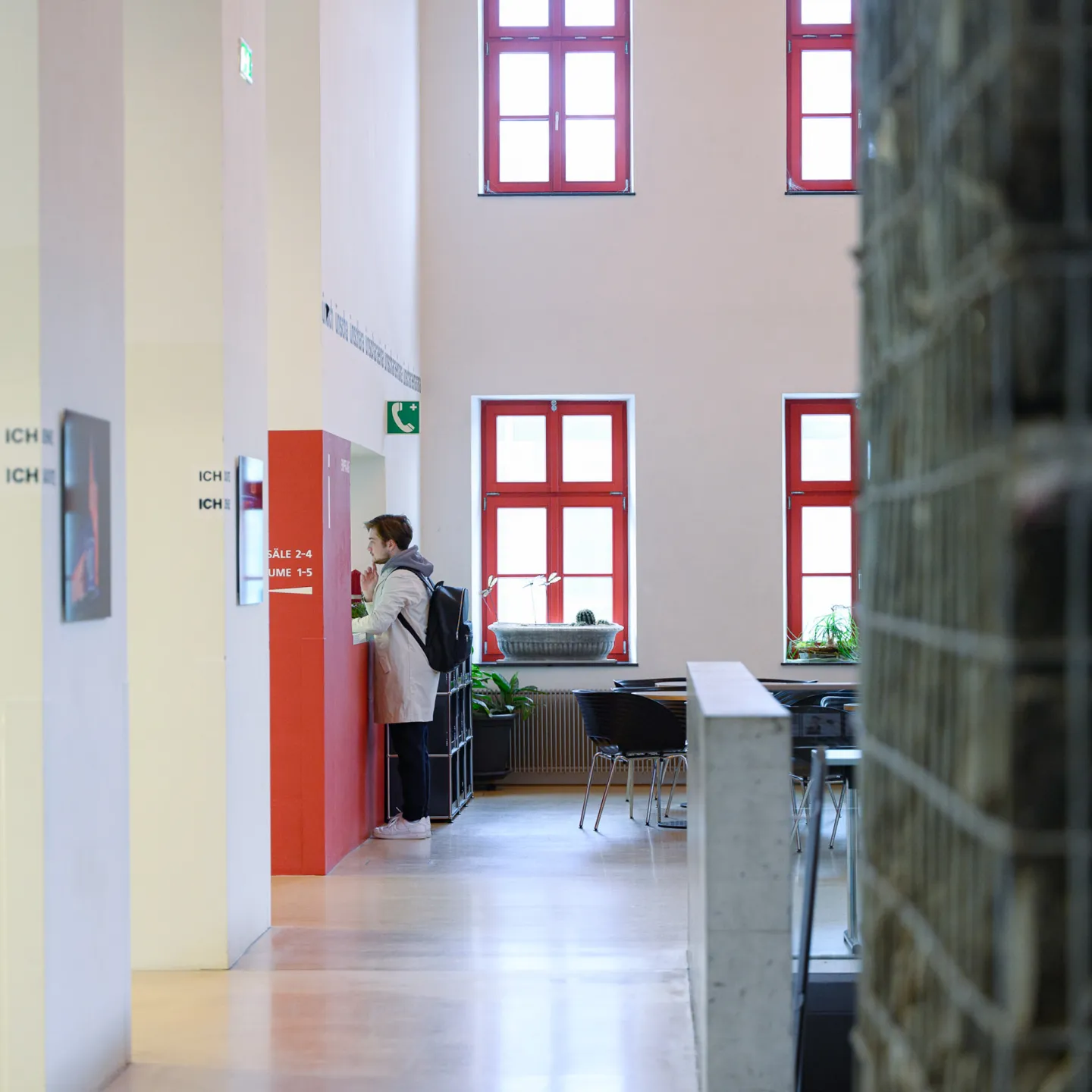 Studierende stehen im Eingangsbereich des historischen Campusgebäudes der Universität Liechtenstein mit auffälligen roten Fenstern.