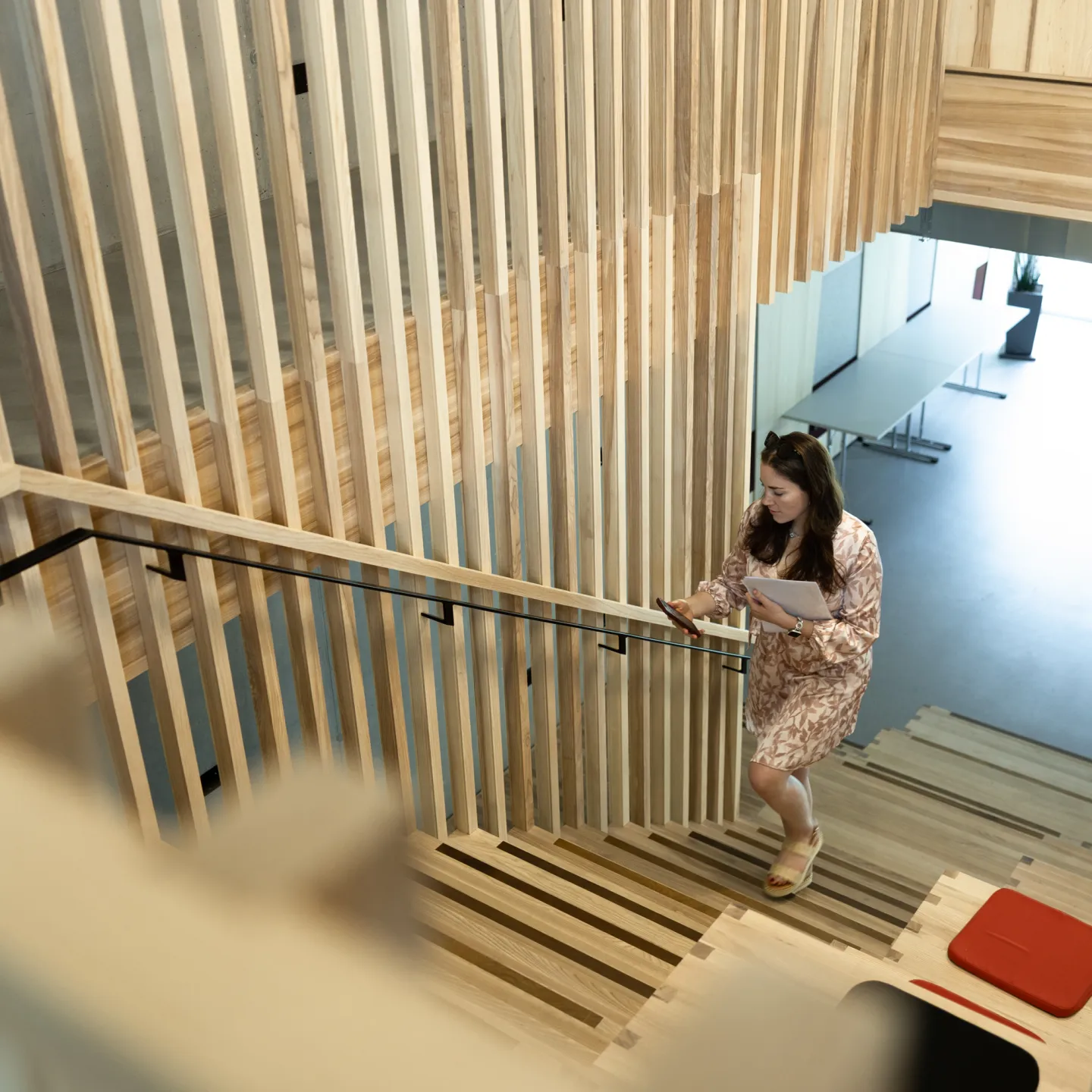 Studentin steigt eine moderne Holztreppe in der Universität Liechtenstein hinauf und schaut auf ihr Smartphone.