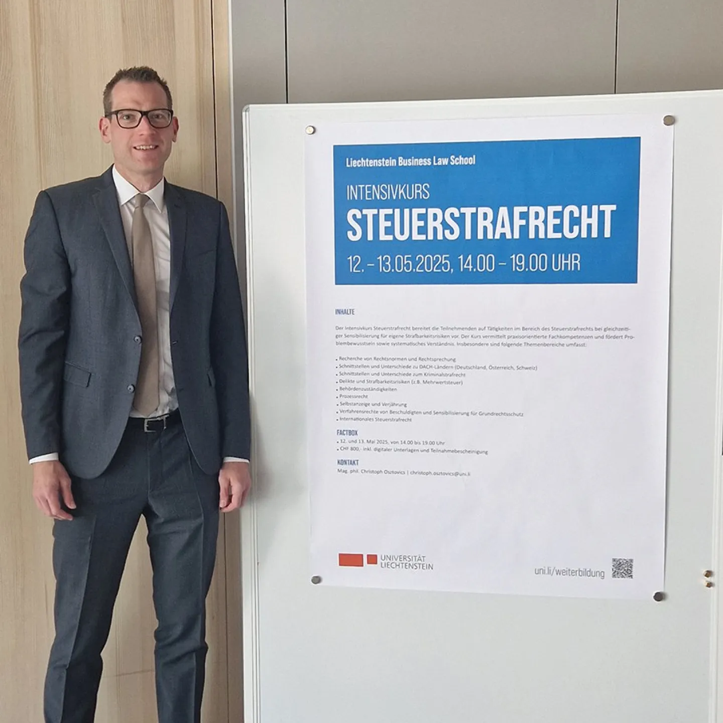 Ein Mann in Anzug steht neben einem Plakat, das den Intensivkurs „Steuerstrafrecht“ der Universität Liechtenstein ankündigt. Das Plakat enthält Informationen zu Datum, Uhrzeit und Inhalten des Kurses.