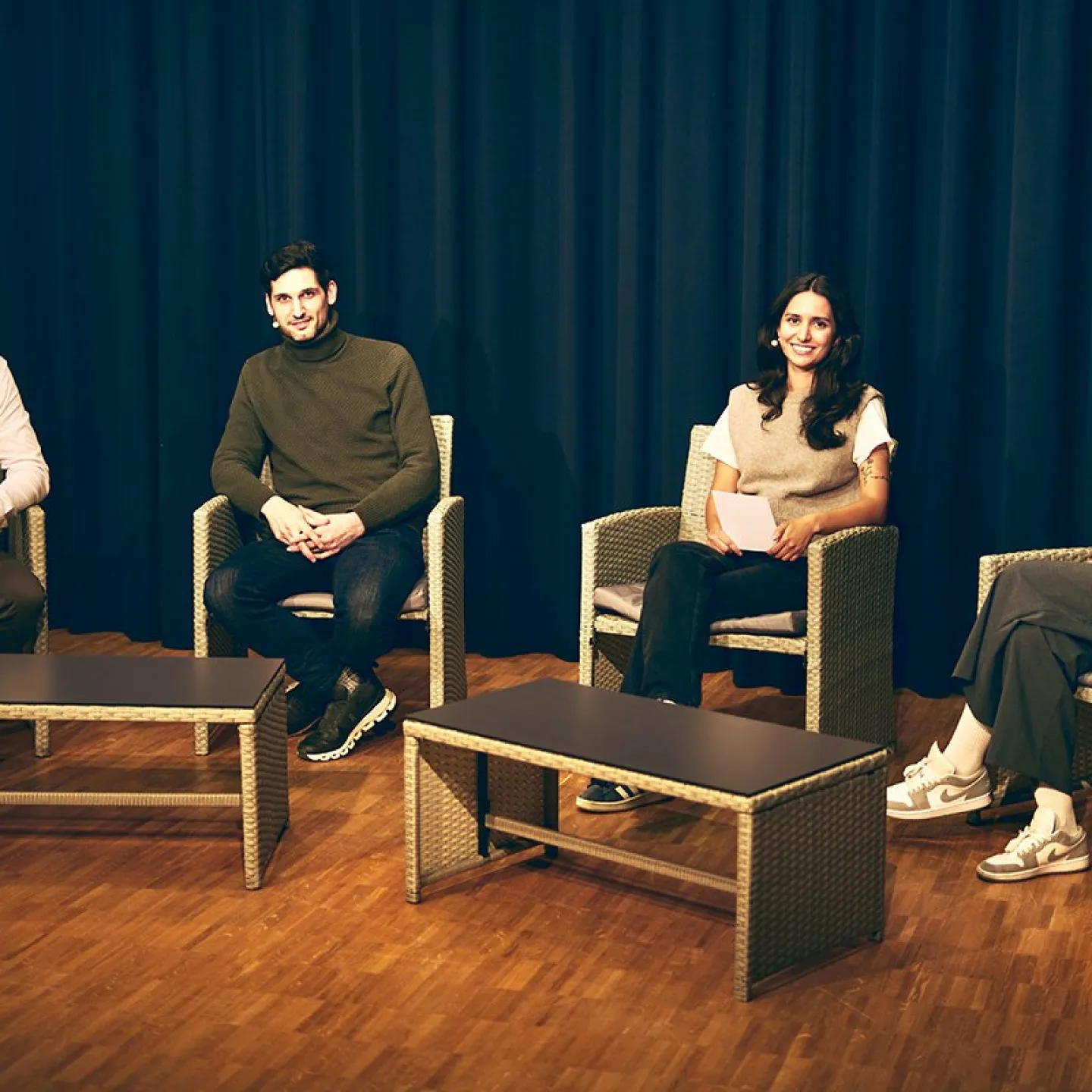 Vier Personen sitzen auf einer Bühne in Korbstühlen, vor einem dunklen Vorhang. Sie sind Teil einer Diskussionsrunde über Upcycling in der Architektur an der Universität Liechtenstein.