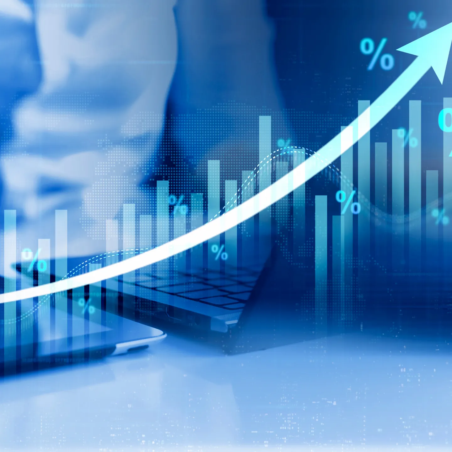 Person analysiert Wirtschaftsdaten an Laptop und Tablet mit steigender Kurve und Prozentzeichen.