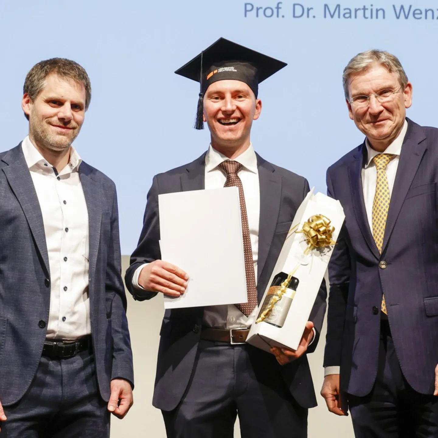 Dr. Christian Frommelt und Prof. Dr. Martin Wenz neben Dr. Kasem Zotkaj mit seinem Diplom.