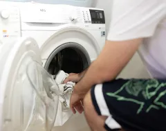 Student lädt weiße Kleidung in eine Waschmaschine im Studierendenwohnheim der Universität Liechtenstein.