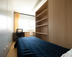 Zimmer im Studierendenwohnheim der Universität Liechtenstein mit Einzelbett, Schreibtisch und Regal.