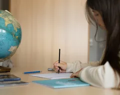 Studentin schreibt an einem Schreibtisch mit Globus im Studierendenwohnheim der Universität Liechtenstein.
