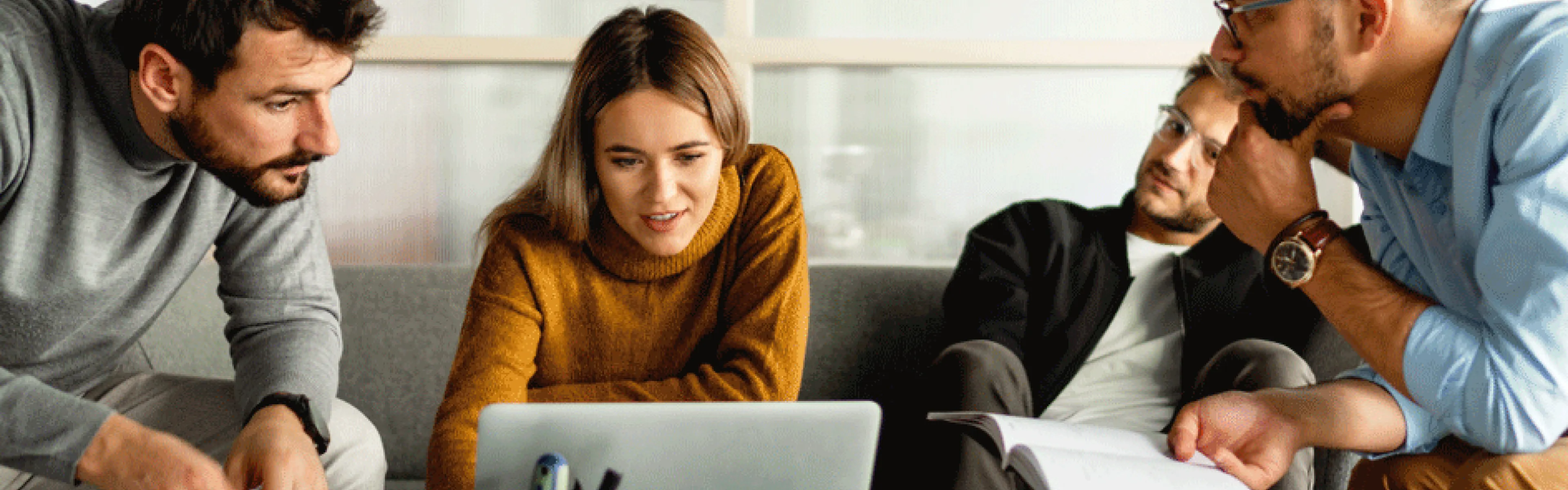 Vier Personen sitzen auf einer Couch und betrachten gemeinsam einen Laptop.