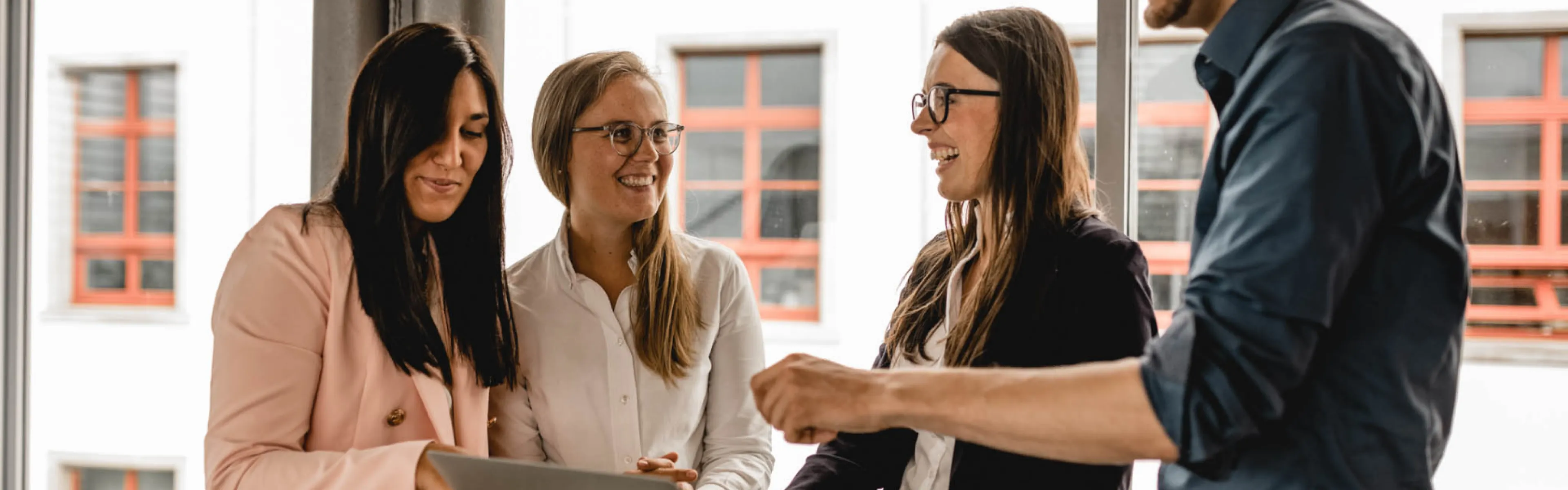 Drei Geschäftsleute stehen um einen Tisch mit einem Laptop und diskutieren gemeinsam über ein Projekt.