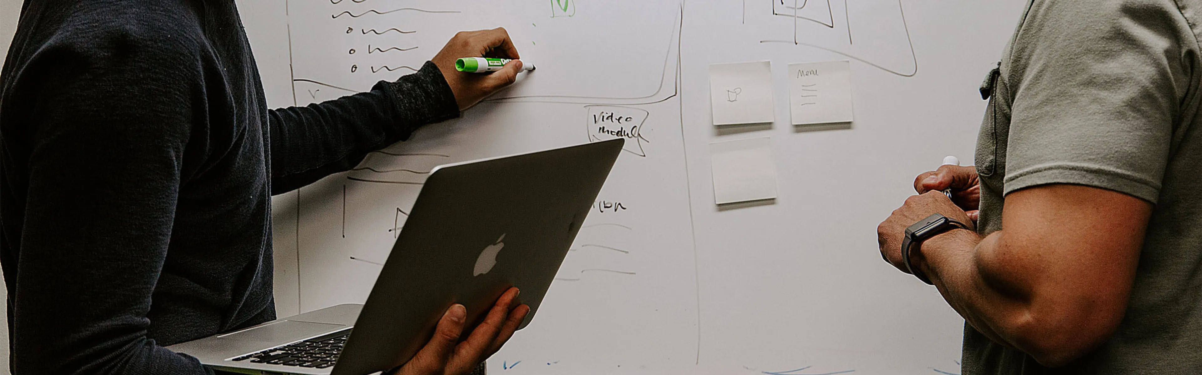 Zwei Personen halten Marker und schreiben auf einer weißen Tafel.