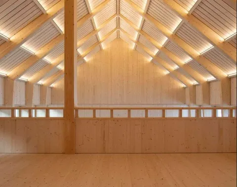 Innenansicht eines modernen Holzgebäudes mit sichtbarer Dachkonstruktion und natürlicher Beleuchtung. Die Architektur betont klare Linien und nachhaltige Materialien.