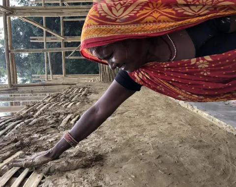 Frau verputzt mit Lehm eine Bambuswand für nachhaltiges Bauprojekt in Südasien