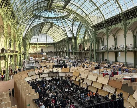 Ein großes, lichtdurchflutetes Konferenzzentrum mit einer beeindruckenden Glas- und Stahlarchitektur. Zahlreiche Teilnehmer sitzen in einem Auditorium, umgeben von Holzstrukturen, die innovative Bauweisen präsentieren.
