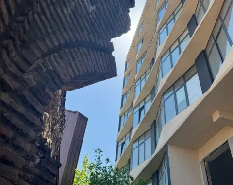 Historische Backsteinmauer im Kontrast zu einem modernen, wellenförmigen Glasgebäude bei Tageslicht.