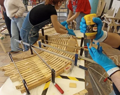 Ein Holzmodell eines Möbelstücks wird von Studierenden zusammengebaut.