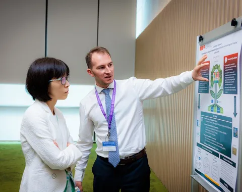 Ein Mann erklärt einer Frau ein wissenschaftliches Poster über nachhaltige Besteuerung in einem Konferenzraum.