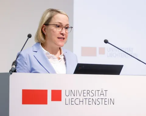 Eine Person hält eine Rede am Rednerpult der Universität Liechtenstein. Im Hintergrund ist das Logo der Universität zu sehen.