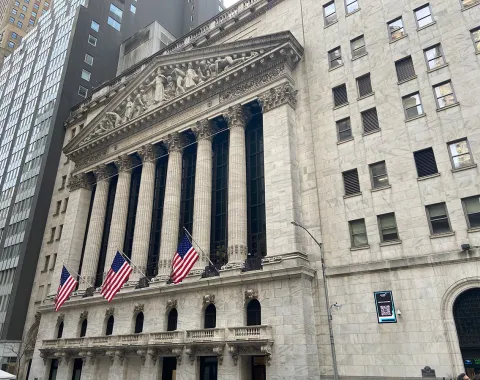 Außenansicht der New York Stock Exchange mit amerikanischen Flaggen, symbolisiert das globale Finanzzentrum und die moderne Finanzwirtschaft.