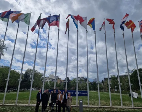Gruppe von Studierenden vor dem Europarat in Straßburg, umgeben von internationalen Flaggen, während einer Studienreise des Executive Master of Laws im Wirtschaftsstrafrecht.
