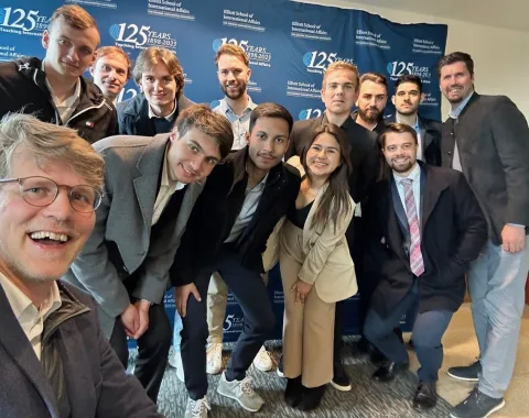 Gruppe von Studierenden und Dozenten der Universität Liechtenstein posiert vor einem Banner der Elliott School of International Affairs während einer Studienreise in den USA.
