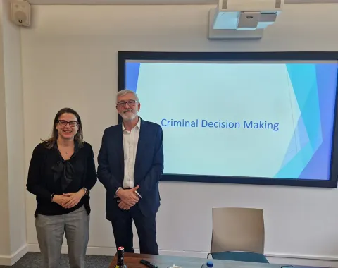 Zwei Personen stehen vor einer Präsentation mit dem Titel "Criminal Decision Making" in einem Seminarraum. Im Hintergrund ist ein Bildschirm mit dem Präsentationstitel zu sehen.