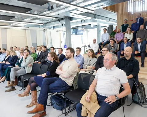 Eine Gruppe von etwa 50 Personen sitzt in einem modernen Konferenzraum und hört aufmerksam einer Präsentation zu. Die Veranstaltung findet an der Universität Liechtenstein statt und thematisiert den Wohnungsmarkt. Im Hintergrund sind einige Personen auf einer Treppe sitzend zu sehen.