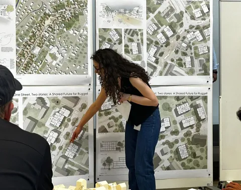 Studentin in Präsentationssituation mit Plänen im Hintergrund