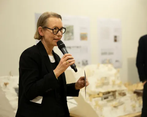 Eine Frau mit schwarzem Sakko und Brille spricht in ein Mikrofon