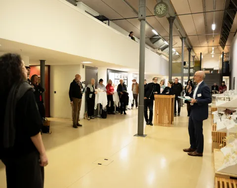 Ein Mann präsentiert vor einer Gruppe von Menschen mit einem Mikrofon in der Hand 